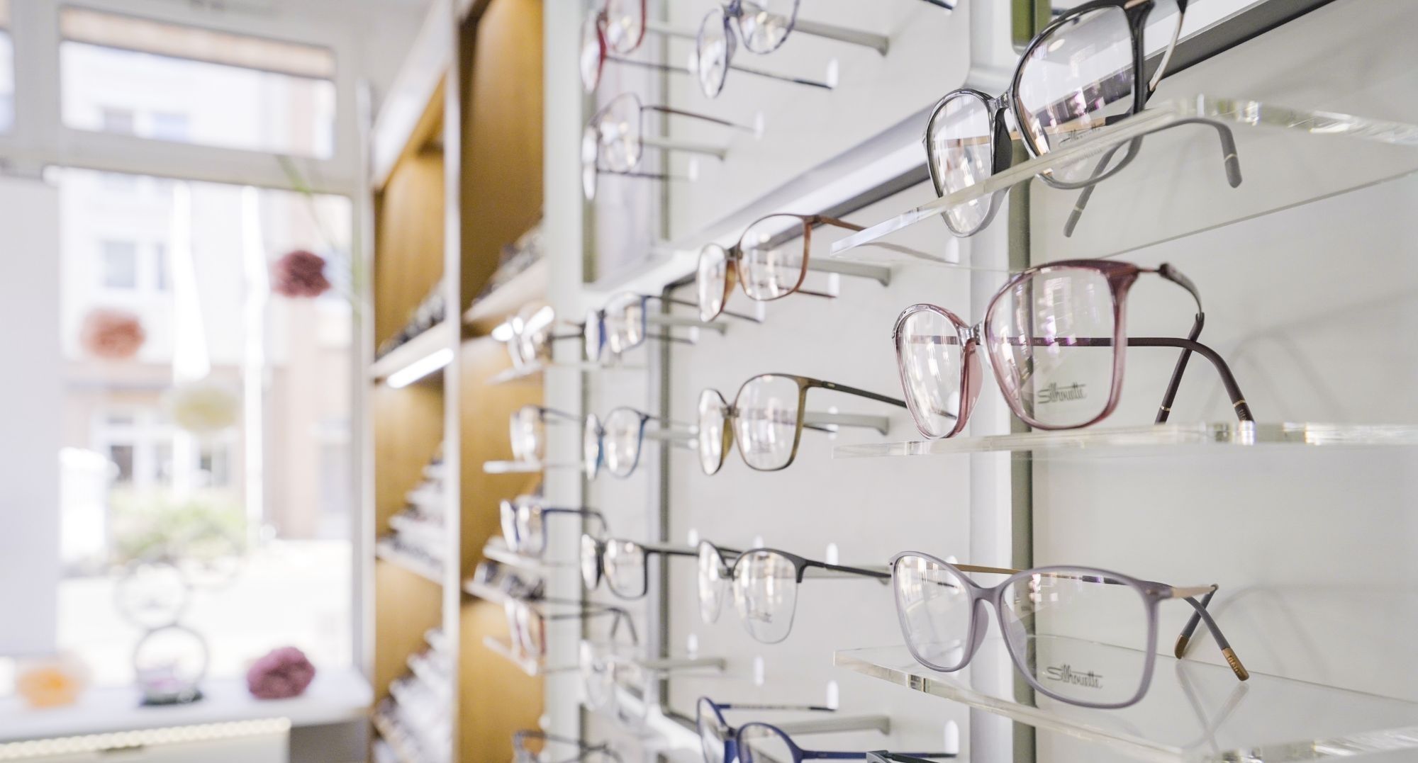 Mehrere Brillenfassungen in verschiedenen Formen und Farben an einer Wandhalterung bei Augenoptik Brückner
