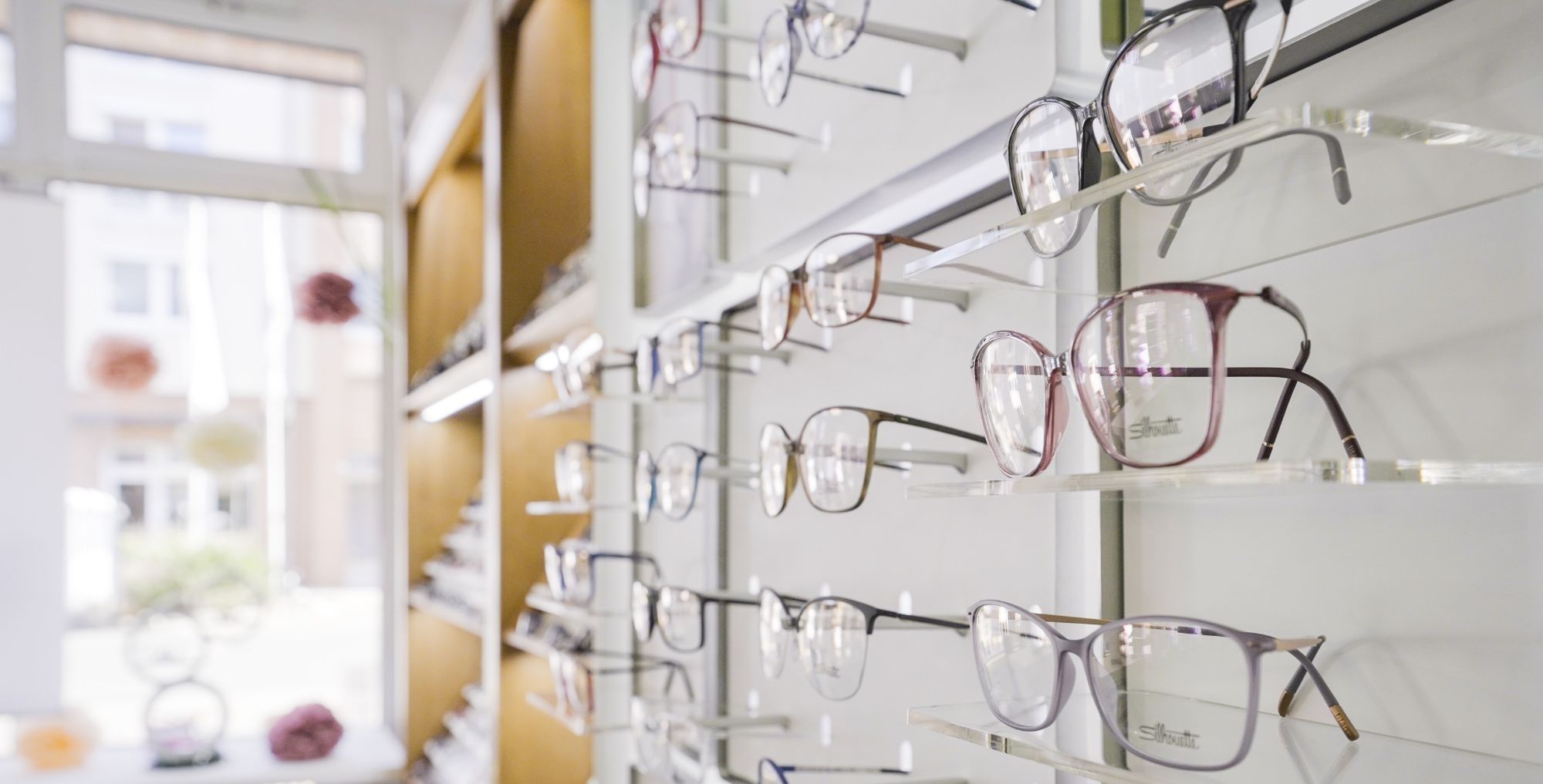 Mehrere Brillenfassungen in verschiedenen Formen und Farben an einer Wandhalterung bei Augenoptik Brückner
